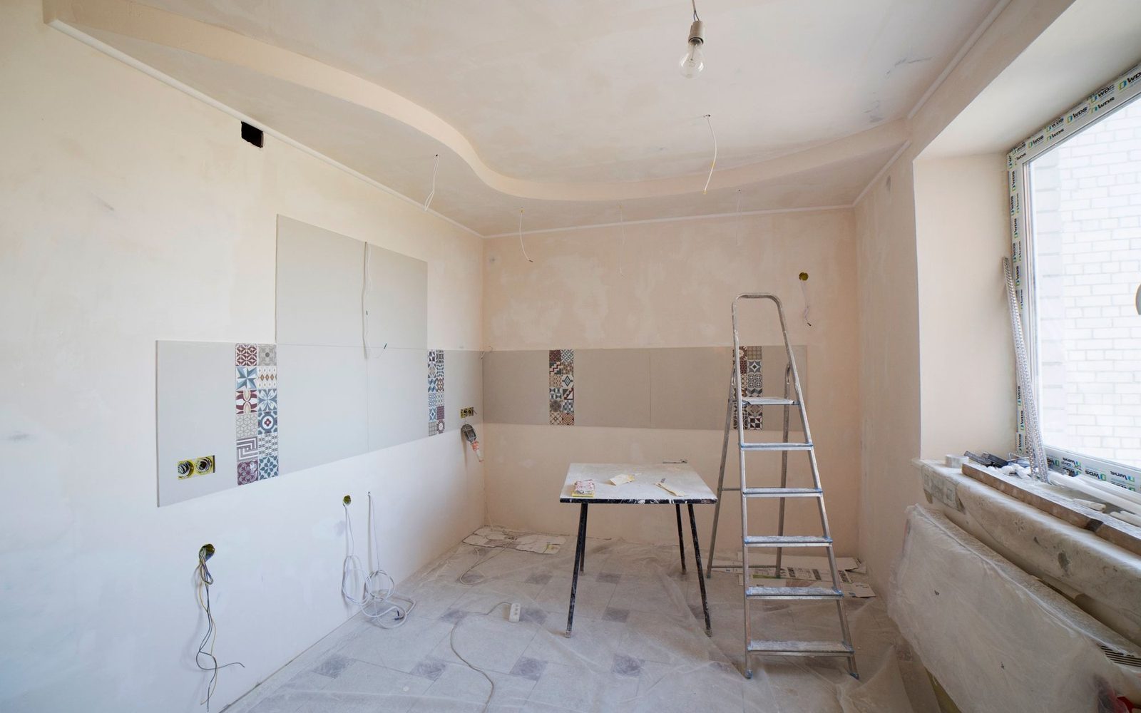 Freshly plastered room with bare walls, a ladder and dust sheets down